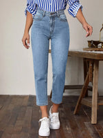 Person wearing blue jeans and a striped shirt in a room with wooden flooring and furniture.