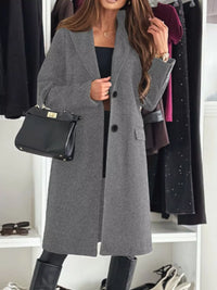 Woman wearing a gray coat with a black handbag in a clothing store.