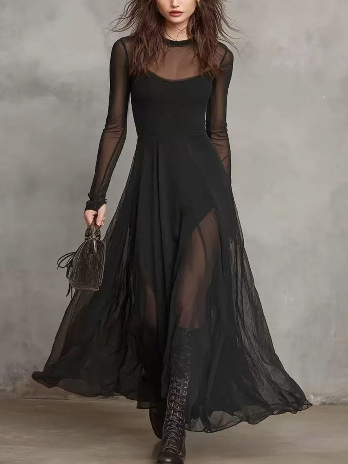 Woman wearing a long black dress with sheer sleeves against a gray background