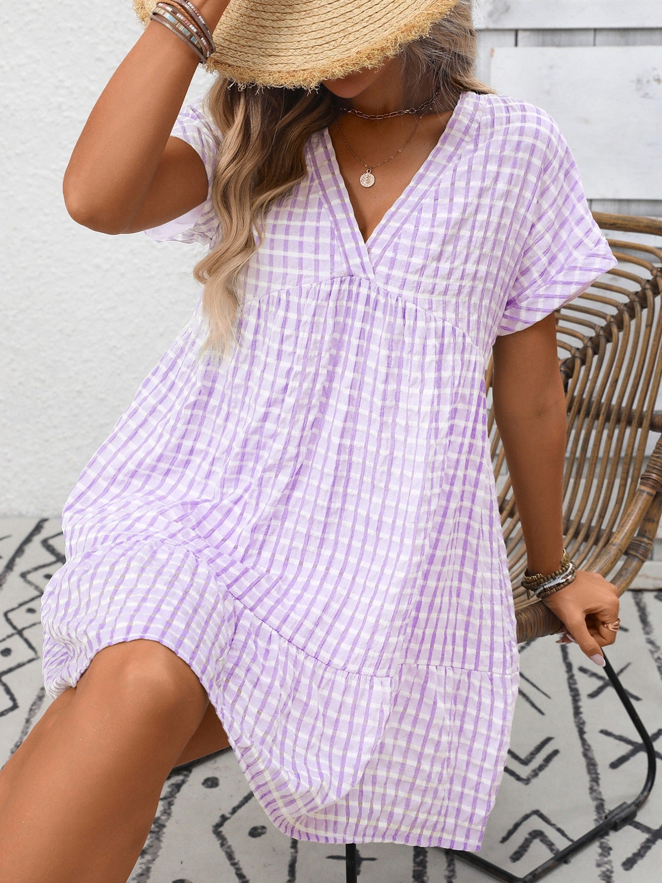 Woman wearing a purple checkered dress sitting on a wicker chair.