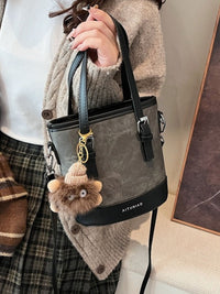 Person holding a gray handbag with a fluffy keychain, wearing a plaid skirt and beige sweater.