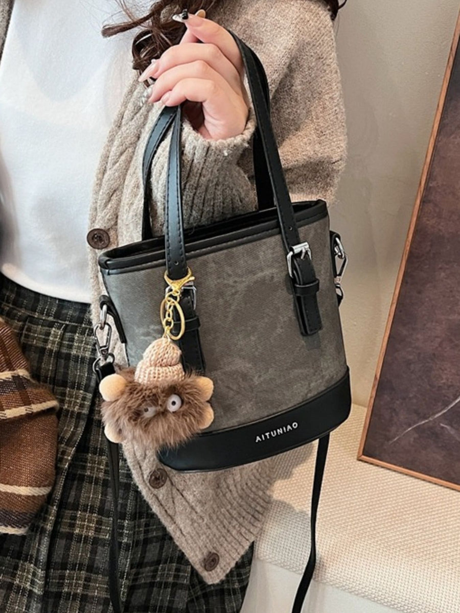 Person holding a gray handbag with a fluffy keychain, wearing a plaid skirt and beige sweater.
