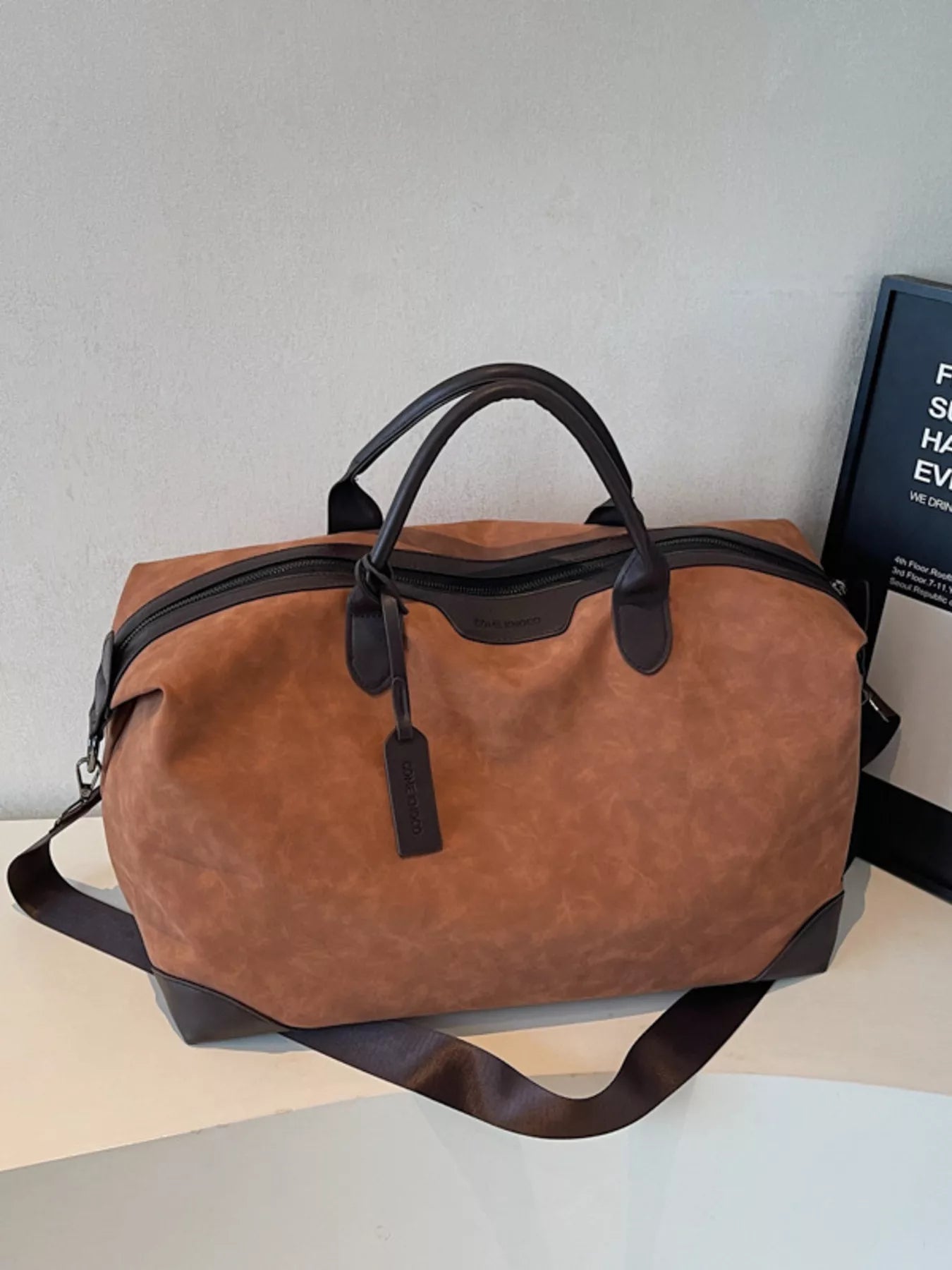 Brown duffel bag with black accents on a light gray surface.