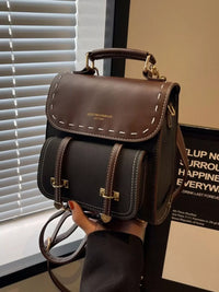 Brown leather satchel bag held by a hand with blinds and a poster in the background
