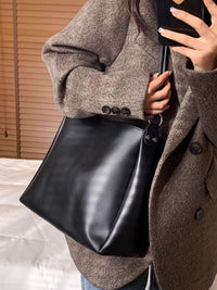 Person wearing a brown coat holding a black handbag.
