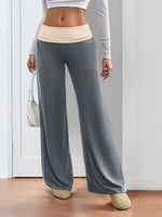 Person wearing gray wide-leg pants and a light-colored top against a white wall.