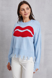 Woman wearing a light blue sweater with a red lip design on a gray background