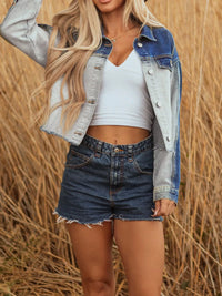 Woman wearing a denim jacket, white crop top, and shorts in a field.
