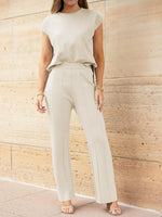 Woman wearing a beige outfit standing against a light brown wall.
