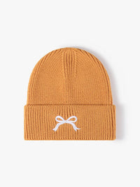 Mustard yellow beanie with a white bow design on a light gray background