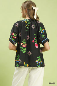 Black blouse with colorful floral patterns worn by a person on a light green background