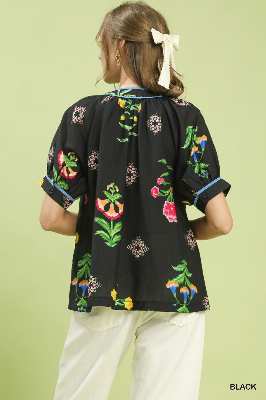 Black blouse with colorful floral patterns worn by a person on a light green background