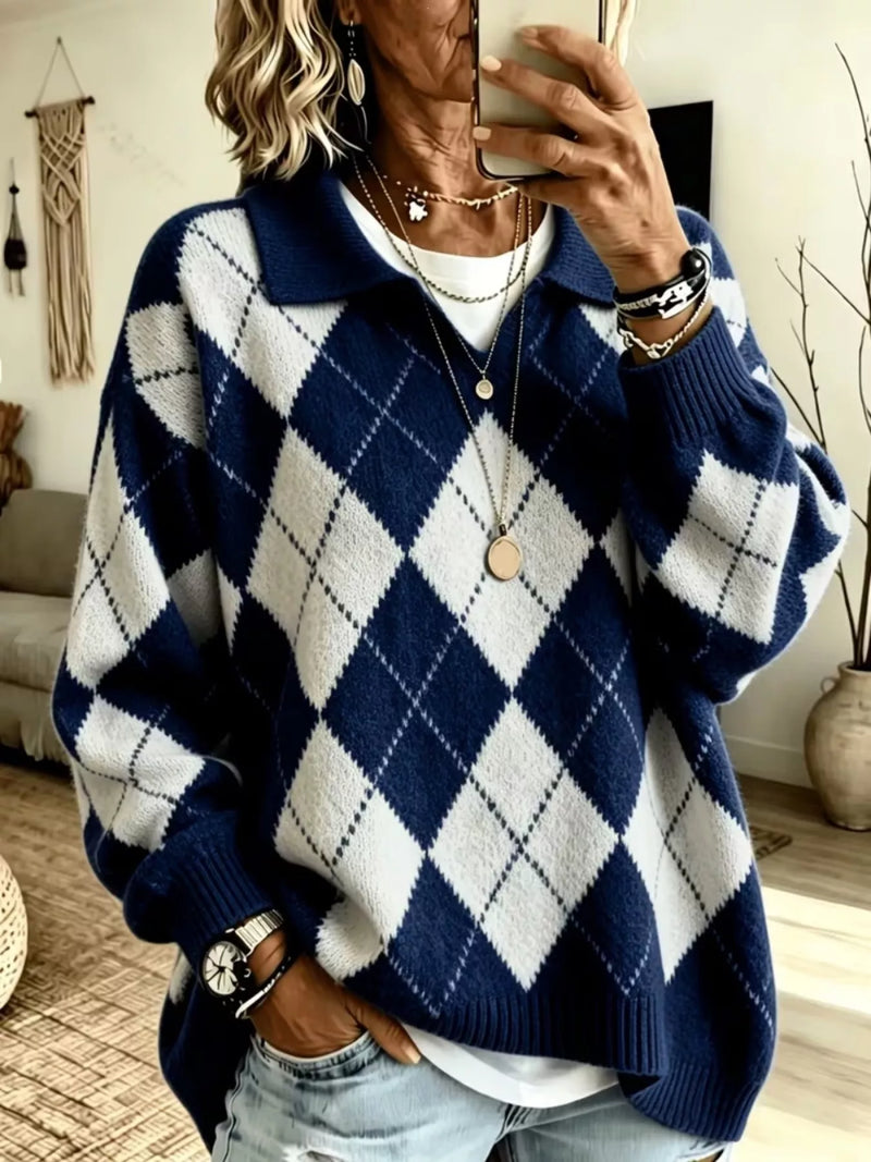 A woman takes a mirror selfie wearing a navy blue and white argyle knit polo sweater, paired with light-wash jeans and layered gold necklaces.
