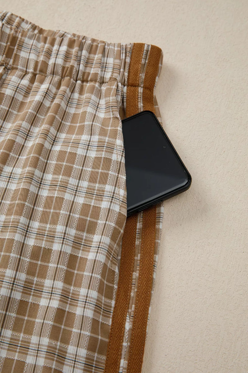 Plaid pants with a brown waistband and a black phone on a beige surface