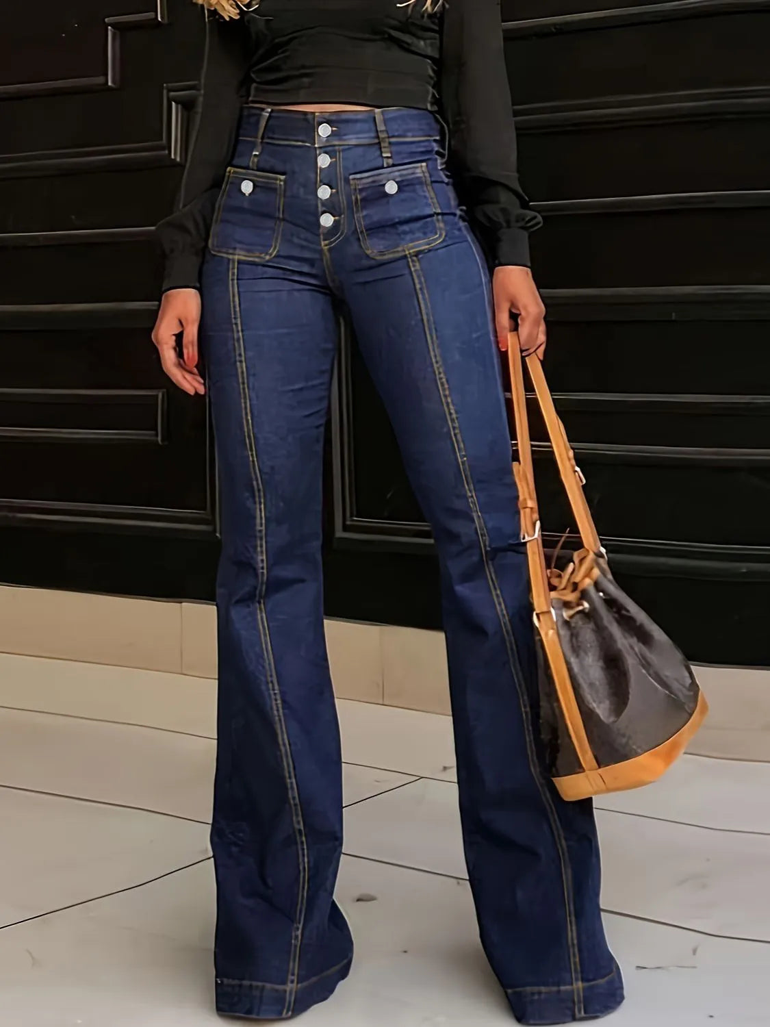 Person wearing high-waisted blue jeans with a black top and carrying a brown handbag.