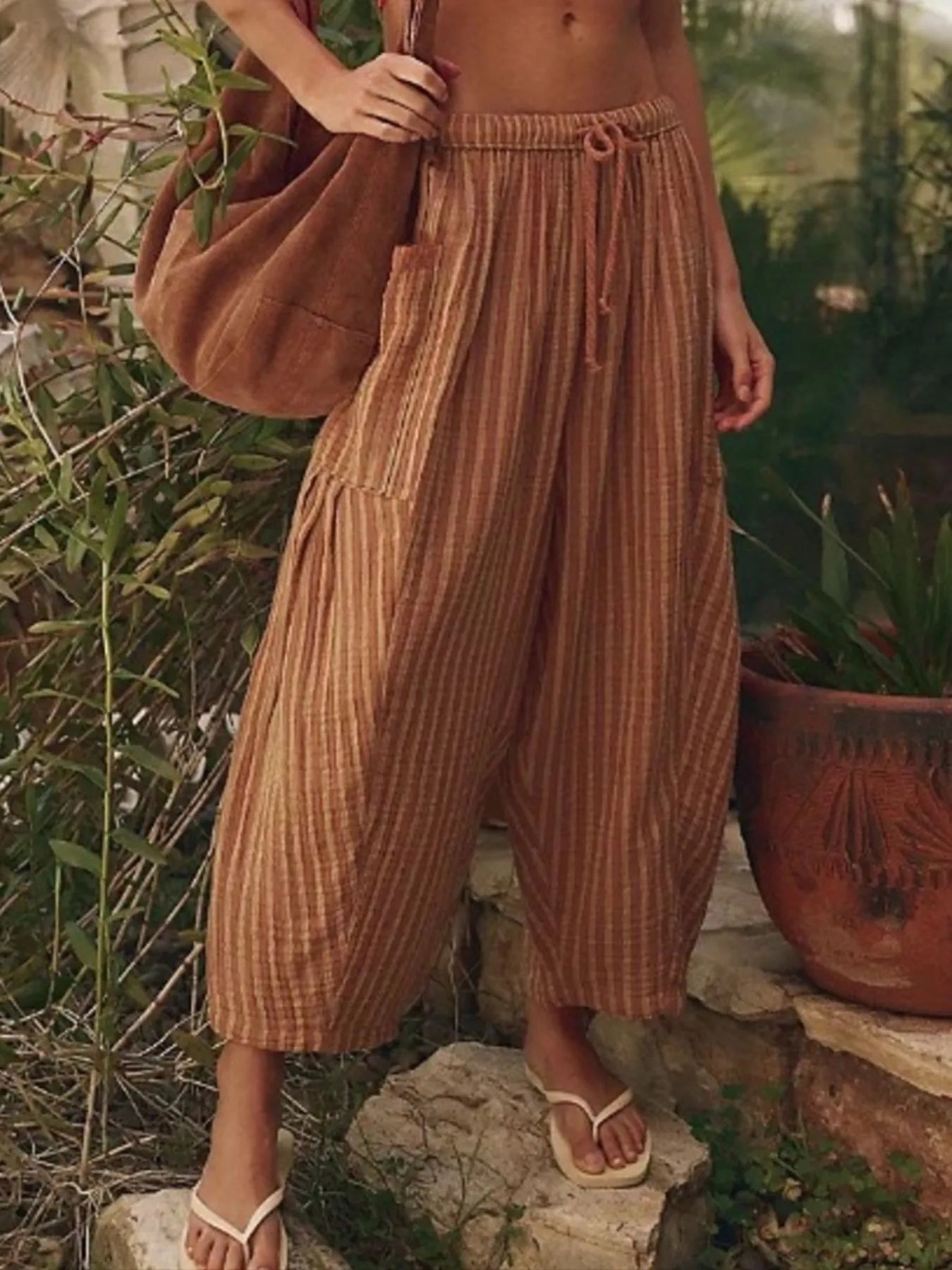 Person wearing brown striped pants and holding a brown bag in an outdoor setting.