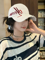 Person wearing a white cap with red text and striped shirt indoors.