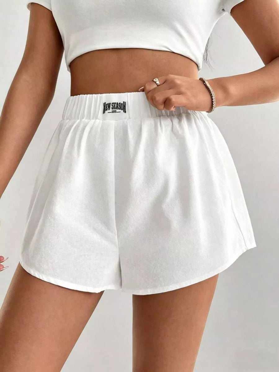 White athletic shorts with a brand logo worn by a person on a light gray background