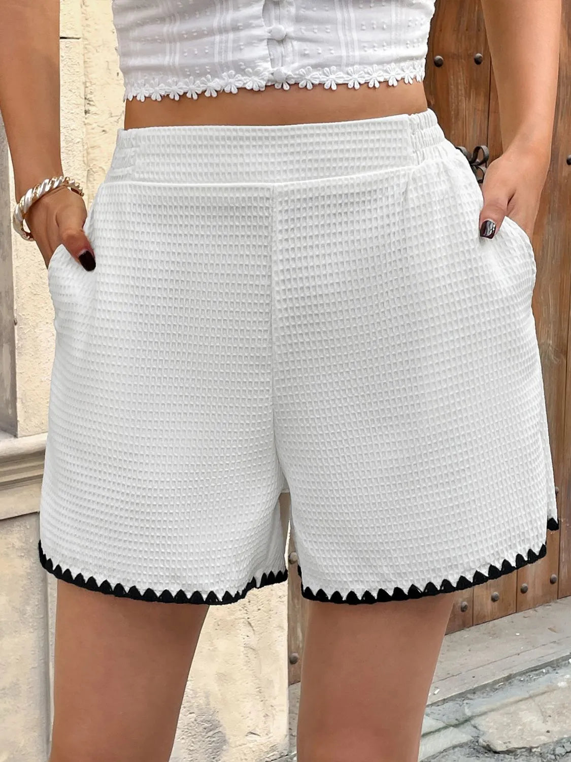 White textured shorts with black trim worn by a person, against a neutral background.