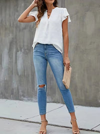 Woman wearing a white blouse and blue jeans against a gray concrete wall.