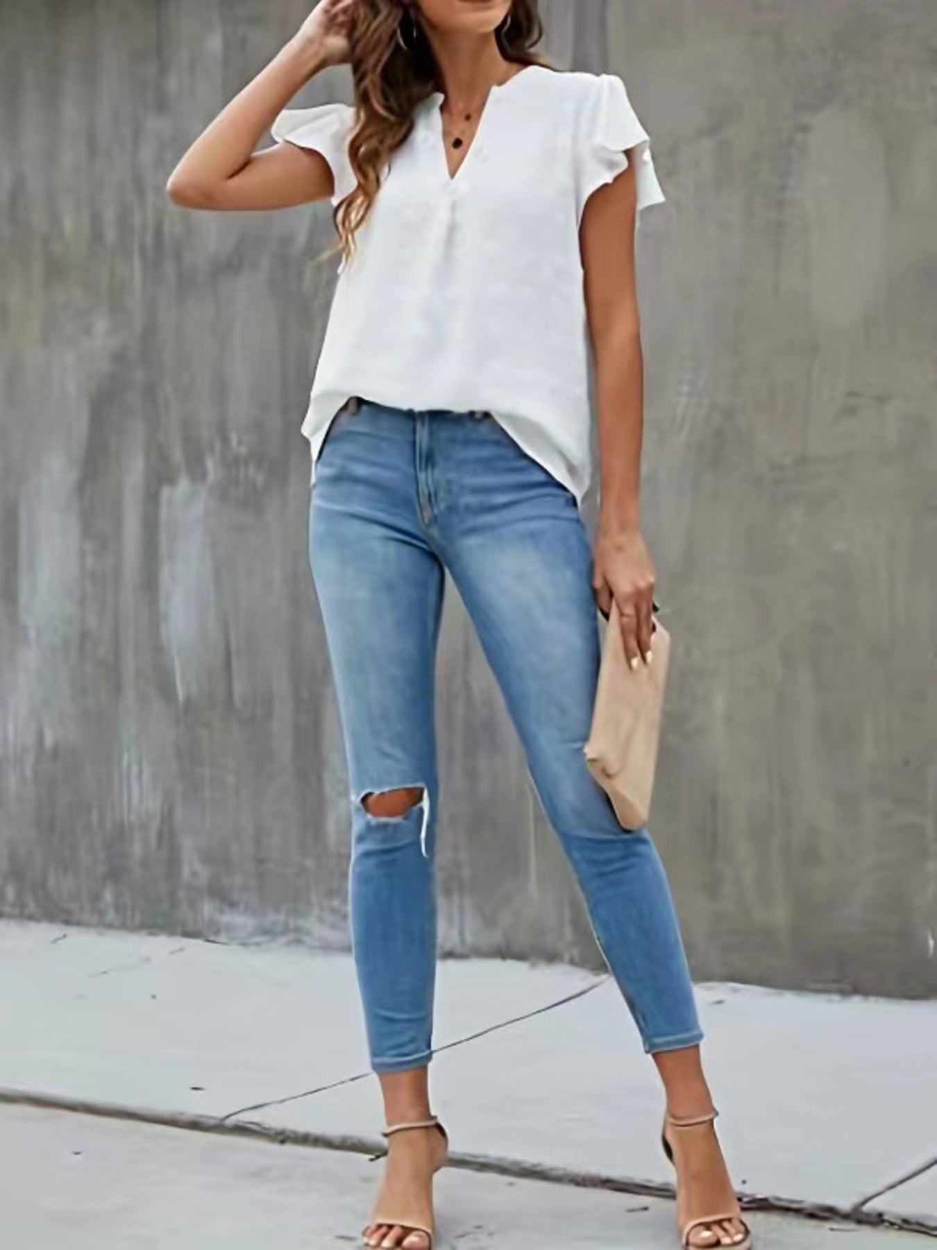 Woman wearing a white blouse and blue jeans against a gray concrete wall.