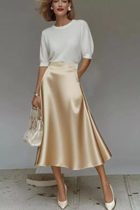 Woman wearing a white top and beige satin skirt with a neutral background