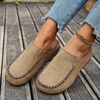 Brown suede loafers worn with denim jeans on a wooden floor.