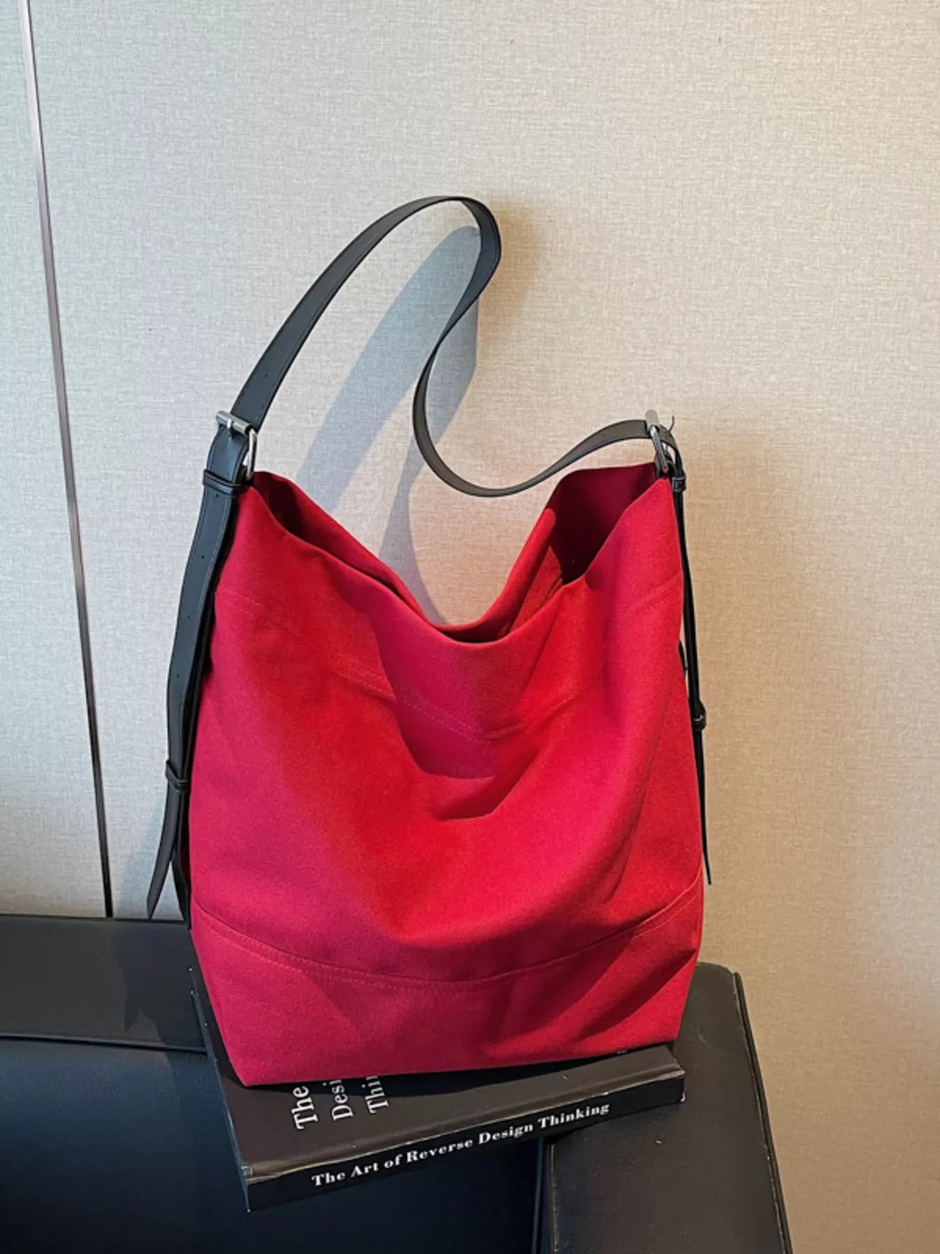 Red handbag with black handle on a book against a neutral wall
