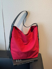 Red handbag with black handle on a book against a neutral wall
