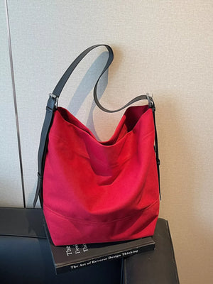Red handbag with black handle on a book against a neutral wall