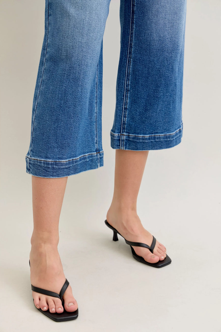 Blue jeans with a rolled hem worn by a person on a light gray background