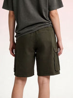 Person wearing olive green cargo shorts on a light pink background