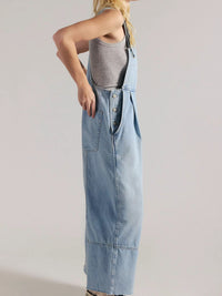 Person wearing a long denim dress over a gray tank top on a plain background