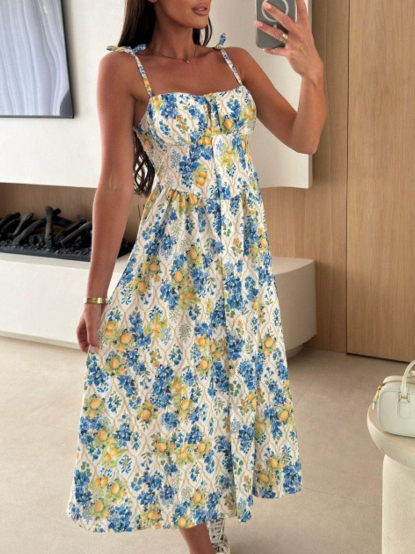 Woman wearing a floral dress taking a mirror selfie in a room.