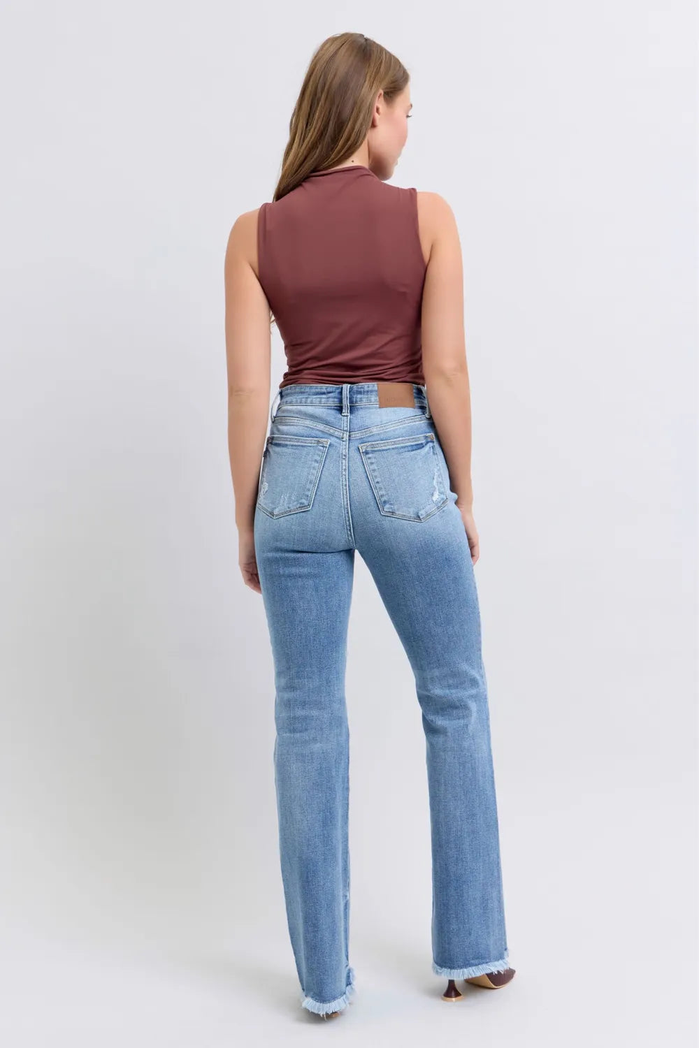 Woman wearing a brown sleeveless top and light blue jeans on a white background