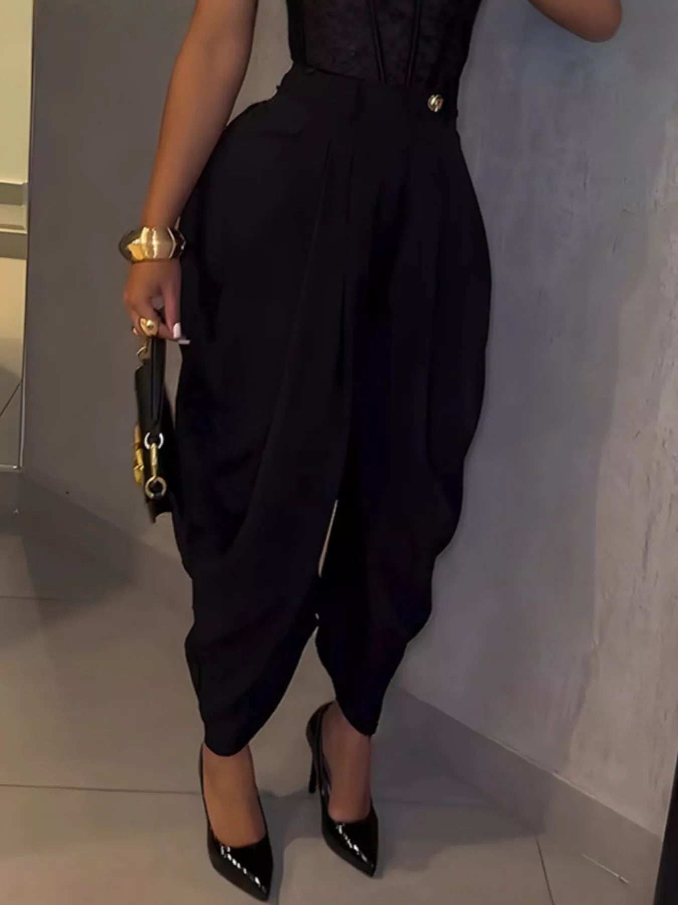 Person wearing a black outfit with high-waisted pants and black shoes, holding a black clutch.