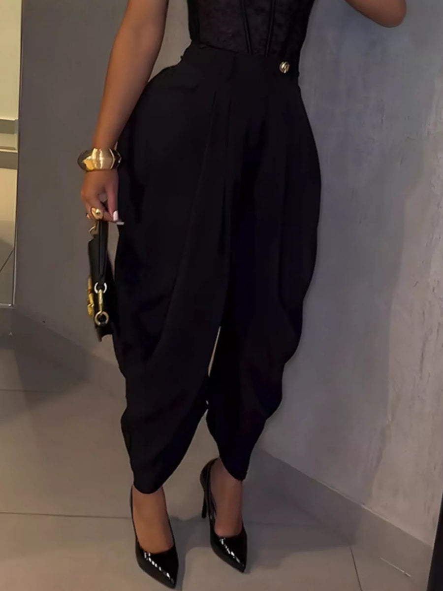 Person wearing a black outfit with high-waisted pants and black shoes, holding a black clutch.