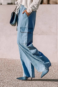 Person wearing light blue wide-leg jeans and a white top, standing against a light-colored wall.