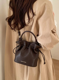 Person wearing a beige coat holding a black handbag with a visible brand logo.