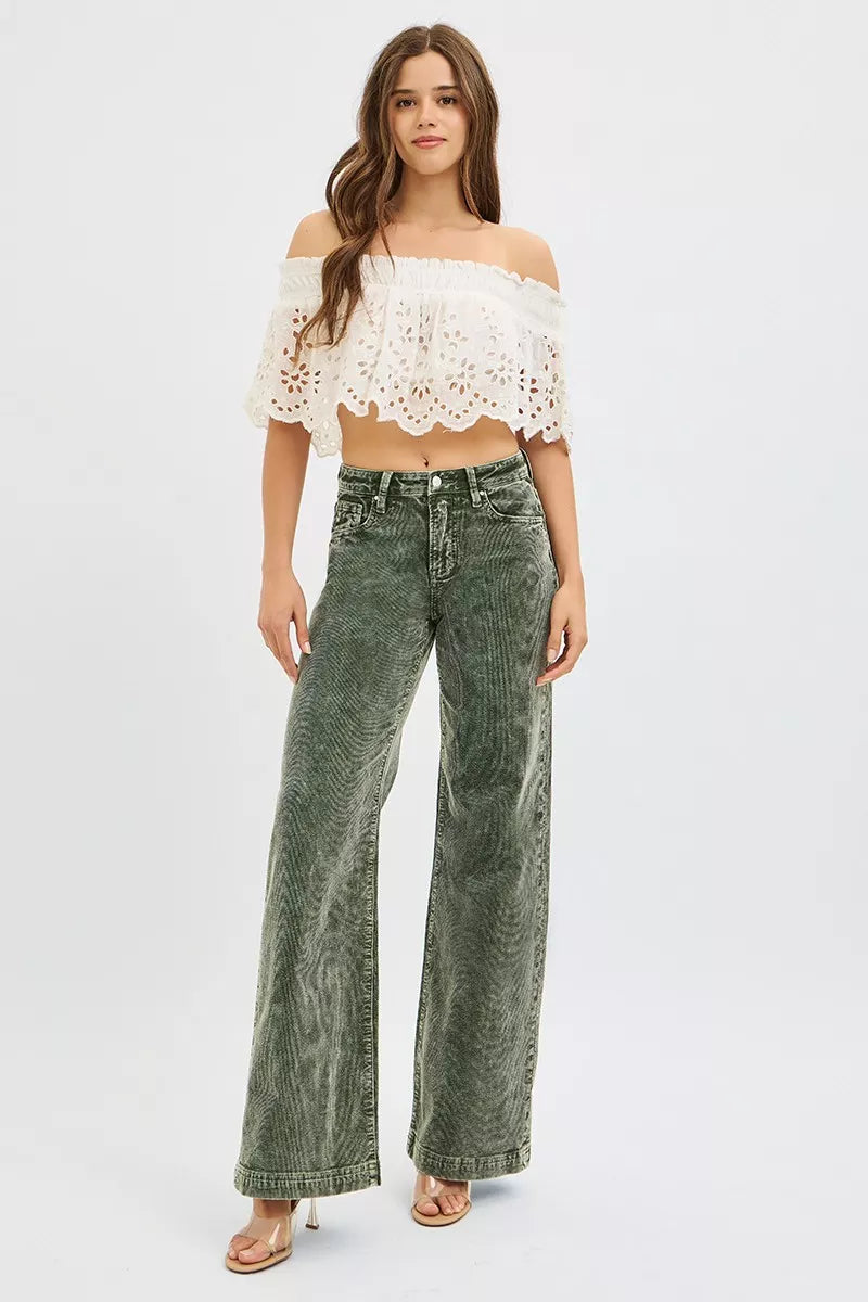 Woman wearing a white lace top and green jeans on a white background