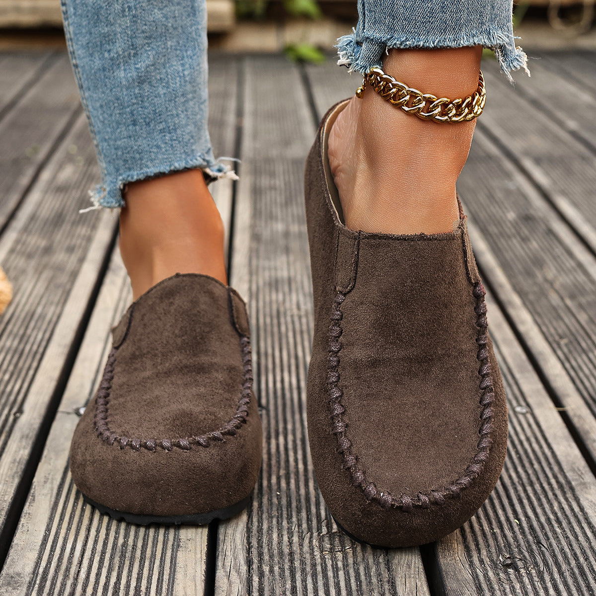 Brown suede loafers worn with ripped jeans on a wooden floor.