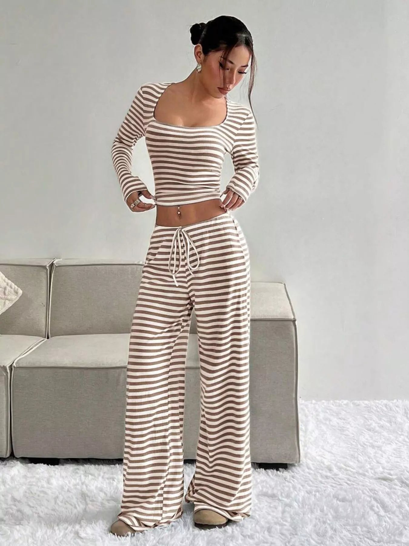 Woman wearing a striped outfit standing in a room with a couch and white carpet.