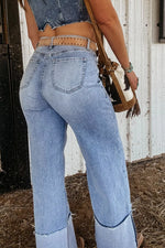 Person wearing light blue jeans with a white wall and black object in the background