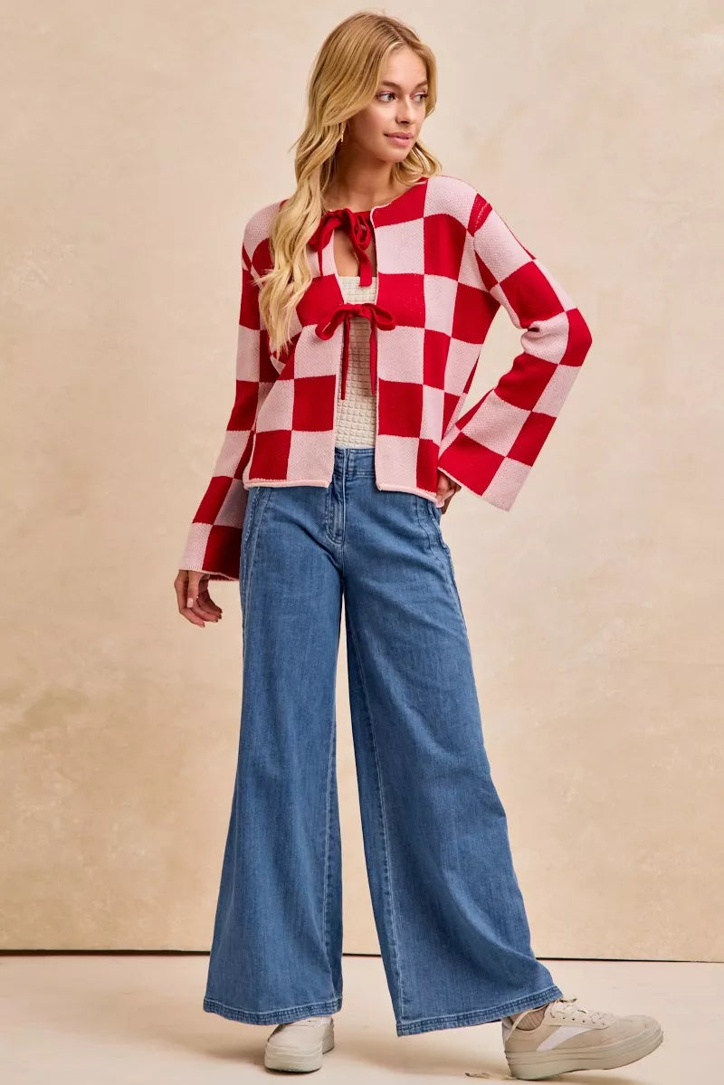 Woman wearing a red and white checkered blouse with a bow and wide-leg jeans on a beige background