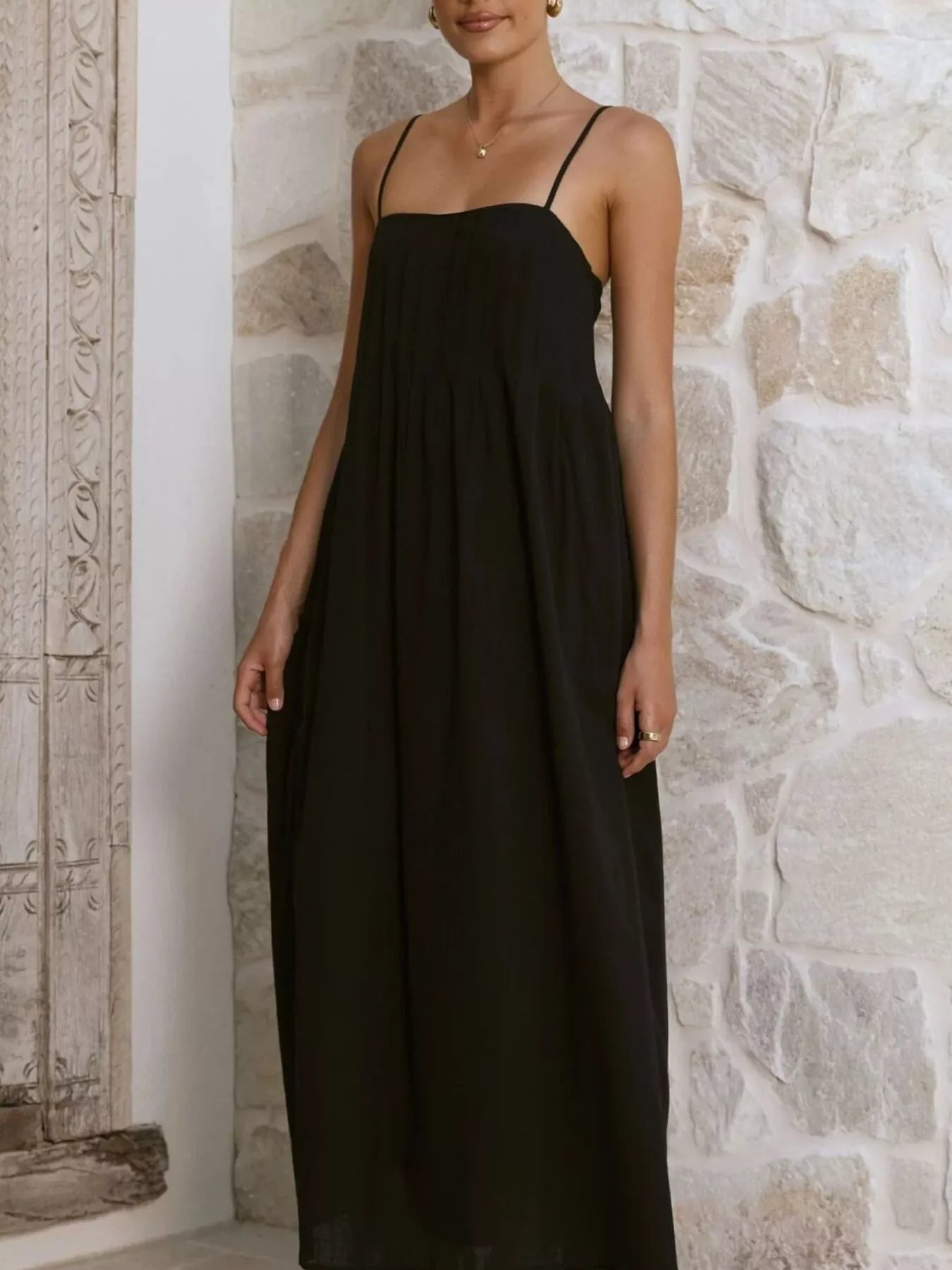 Woman wearing a black dress against a stone wall.