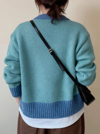 Person wearing a teal sweater with a black strap over their shoulder against a beige background