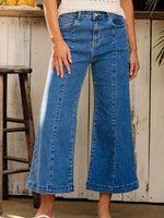 Person wearing blue jeans standing in a rustic setting with wooden furniture and a white wall.