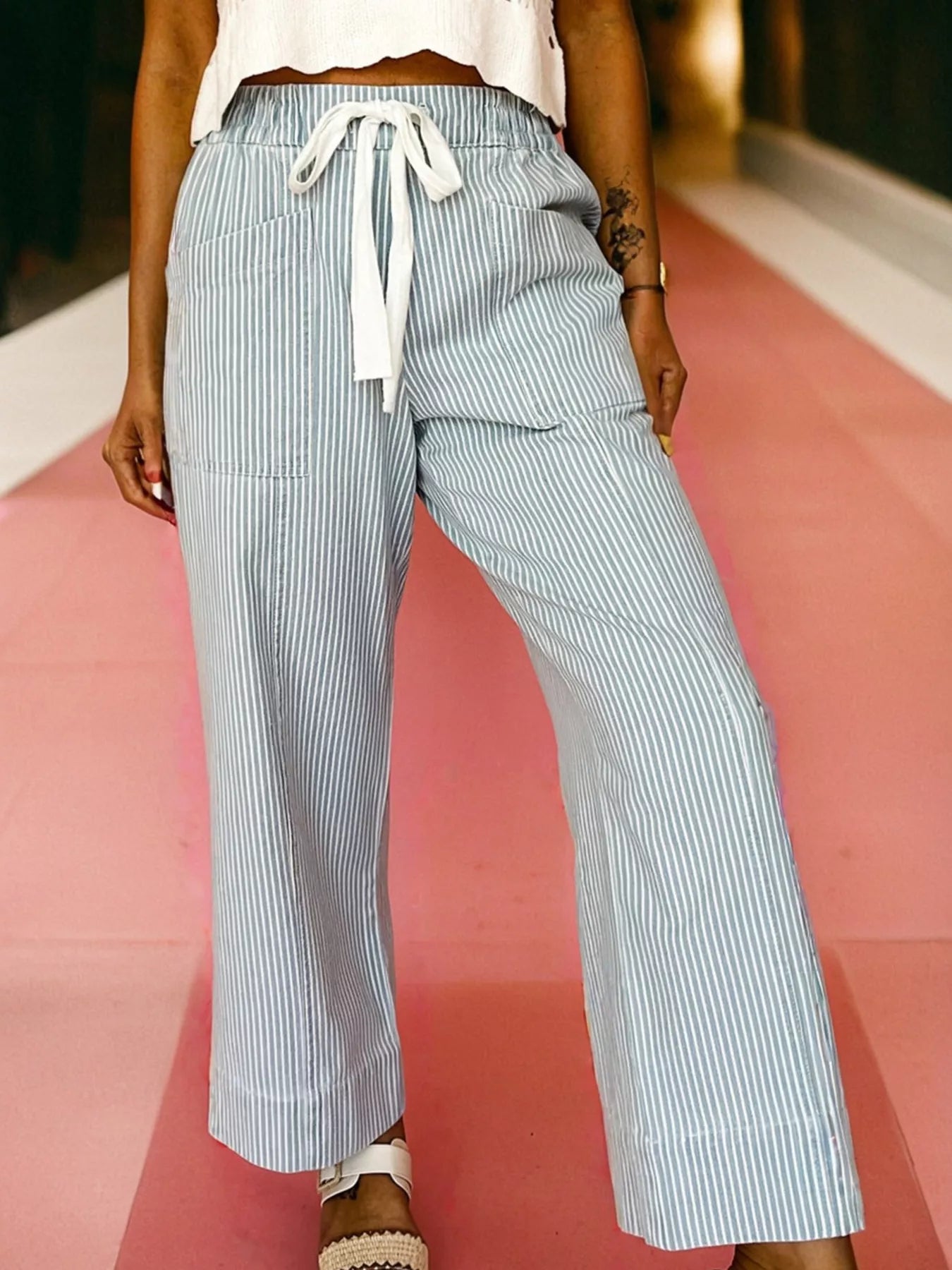 Person wearing light blue and white striped pants on a pink and white background