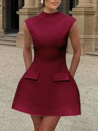 Woman wearing a maroon dress with a textured pattern in front of a building entrance.