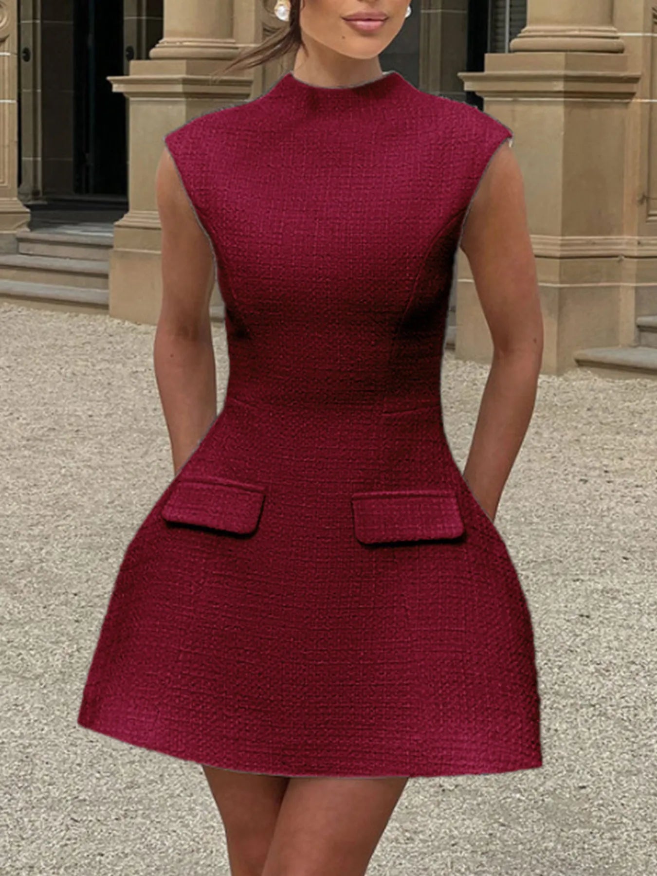 Woman wearing a maroon dress with a textured pattern in front of a building entrance.